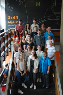 Sigrun Seifert (1. Reihe, re.), Jörn Kommnick (2. Reihe, re.), Katharina La Rocca (3. Reihe, re.), Norbert Richter (4. Reihe, re.) und Schulleiterin Simone Waltermann (5. Reihe, re.) zusammen mit den angehenden Augenoptikerinnen und Augenoptikern, die hier mit großer Freude eine EinDollarBrille tragen.